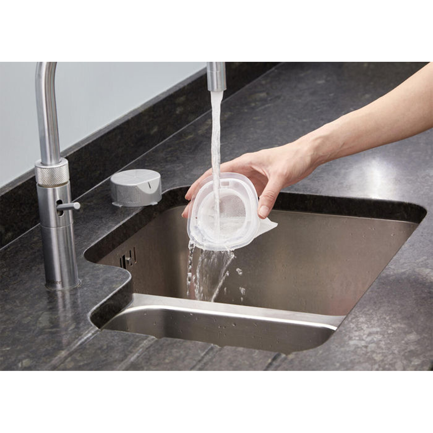 Una mano che risciacqua un filtro in un lavello da cucina in acciaio inossidabile.