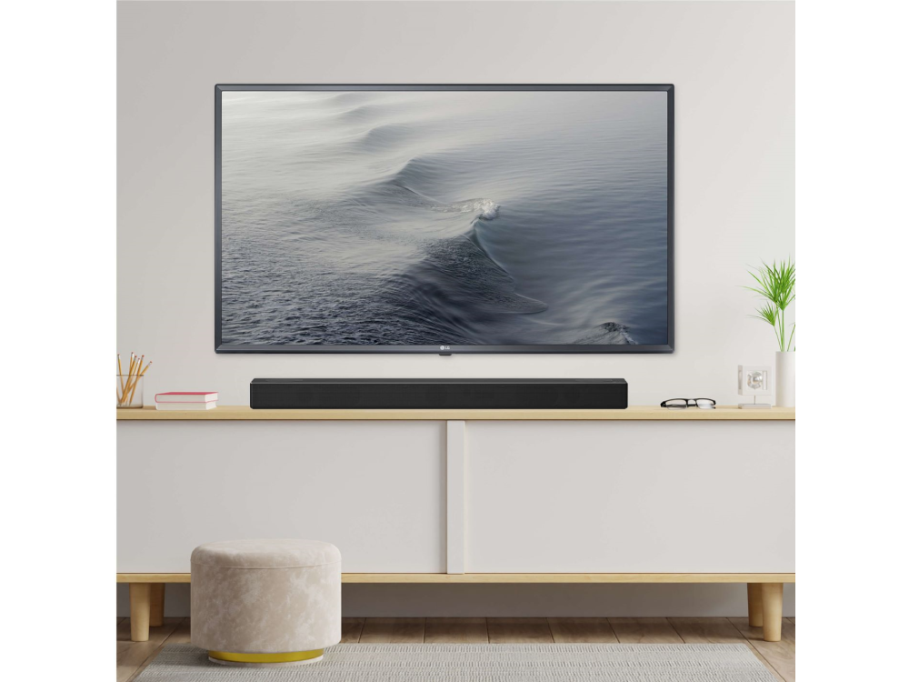 Sala de estar con TV, barra de sonido y gabinete blanco. Hay un taburete y decoración.
