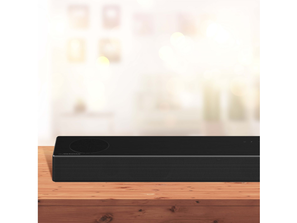Barra de sonido negra sobre mesa madera con fondo borroso. Equipo de audio doméstico.