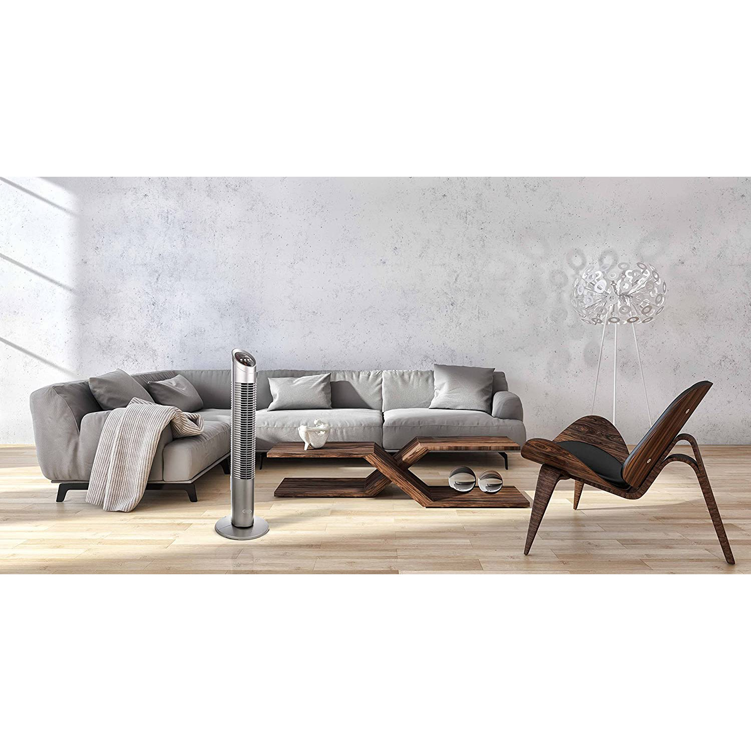 Soggiorno con divano grigio, tavolino in legno, ventilatore alto e sedia.