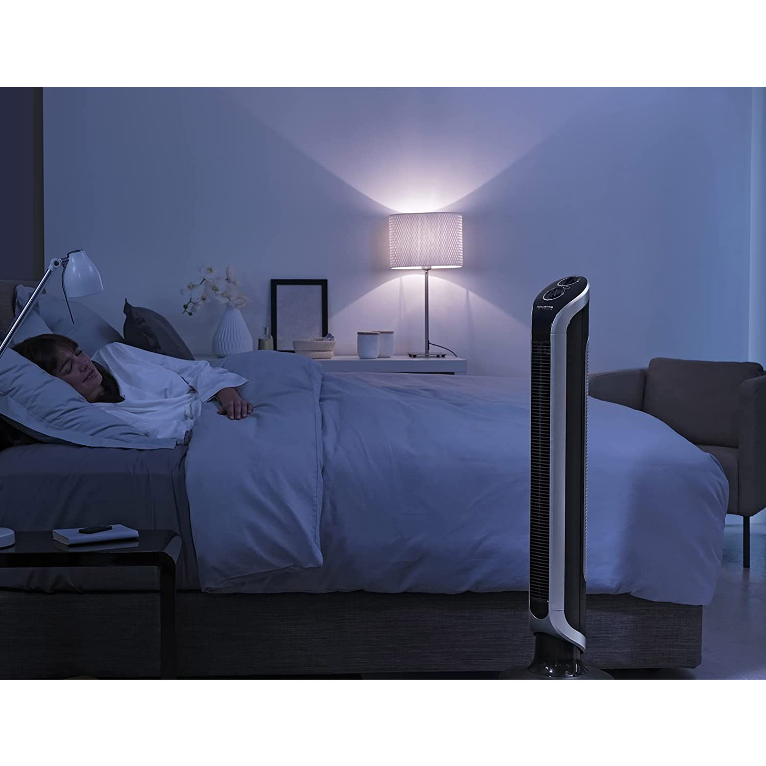 Scena di camera da letto, donna a letto, lampada e ventola, ambiente tranquillo.