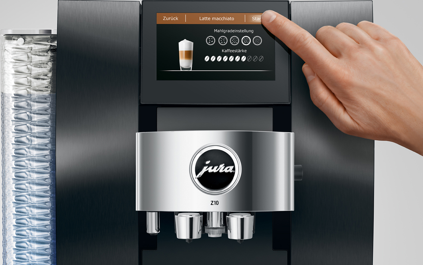 La mano di una persona preme il pulsante di avvio su una macchina da caffè nera e argento. Una bevanda al caffè è sullo schermo.