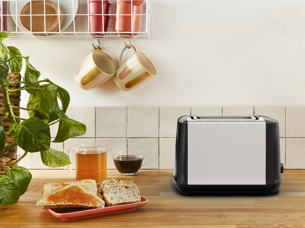 Tostadora, tostadas, té y café en una mesa de madera. Plantas y tazas están allí.