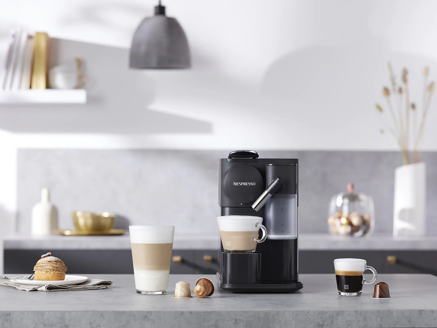 Kaffeemaschine mit zwei Kaffeetassen und einem Glas Latte mit Gebäck.