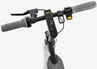 Gros plan sur un guidon de scooter. Il a des poignées grises, un écran noir affichant '0' et un levier. Le fond est blanc.