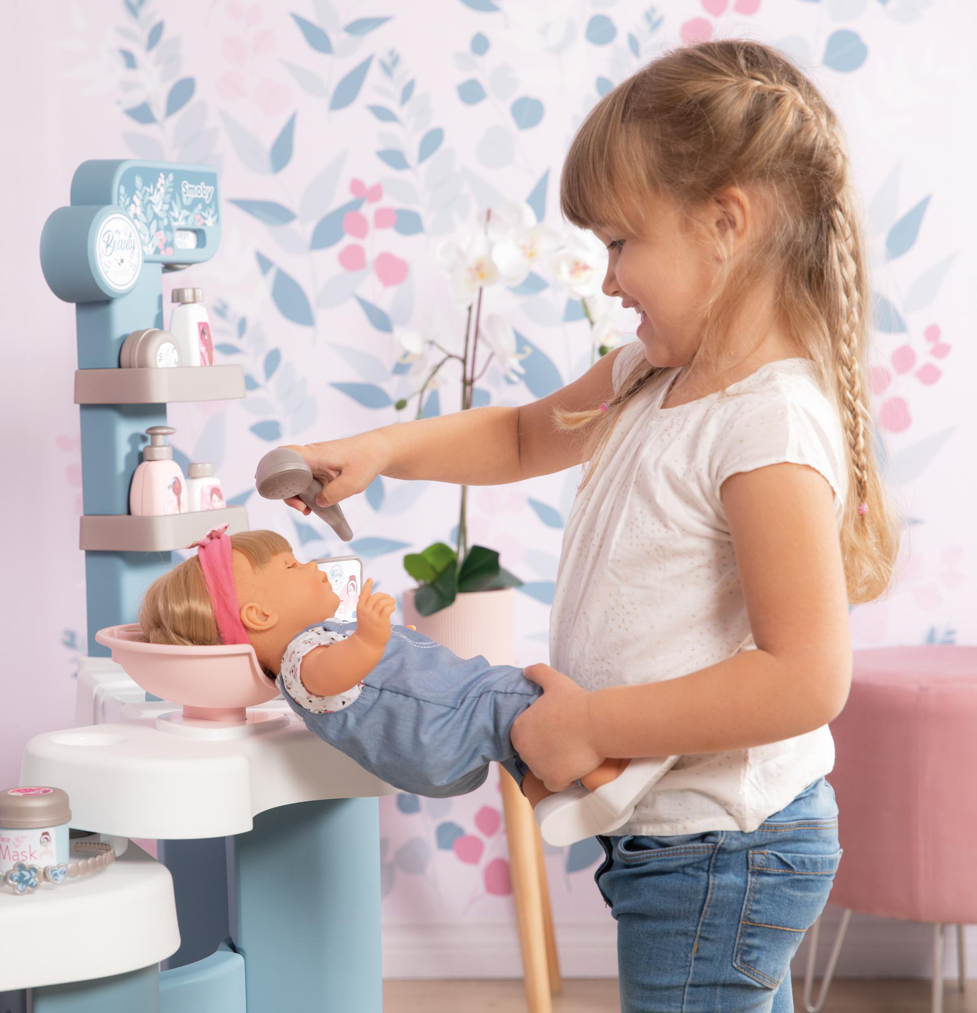 Ein Mädchen spielt mit einer Puppe in einem Salon, hält ein Mikrofon vor das Gesicht der Puppe.