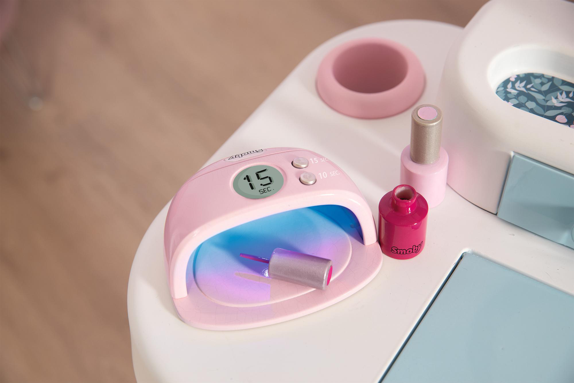 Rosa Nageltrockner mit einer Nagellackflasche auf einem weißen Tisch.