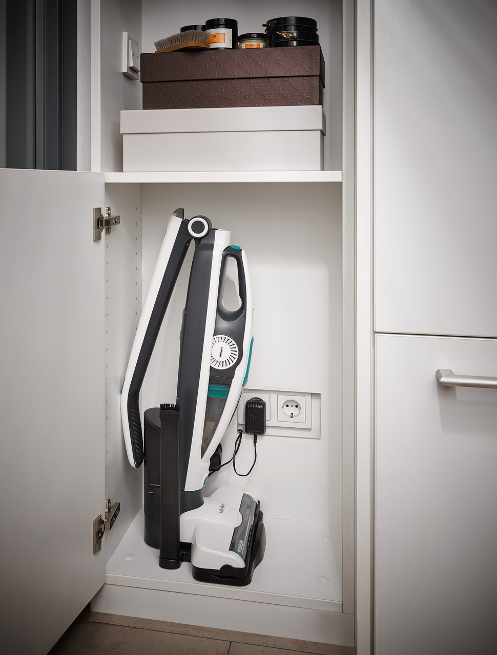 Aspirateur rangé dans une armoire blanche. L'armoire a des étagères au-dessus.