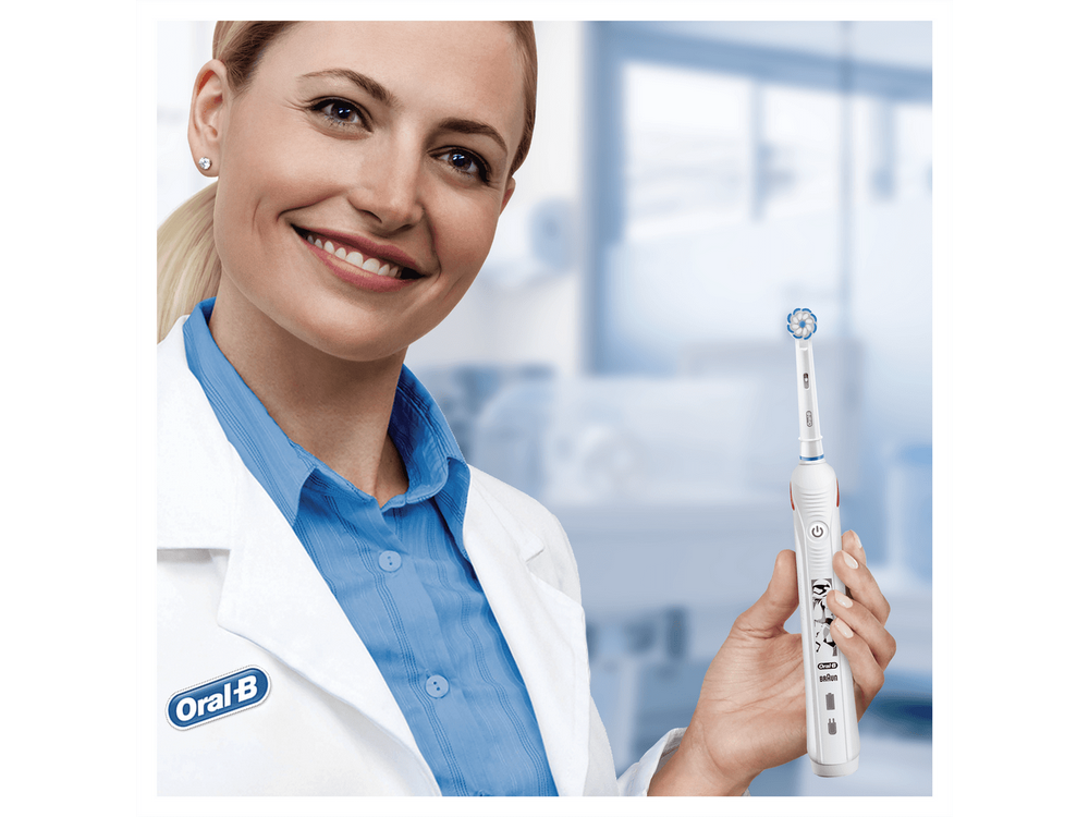 Mujer con bata de laboratorio sostiene un cepillo de dientes eléctrico. Sonríe al espectador. Fondo azul.