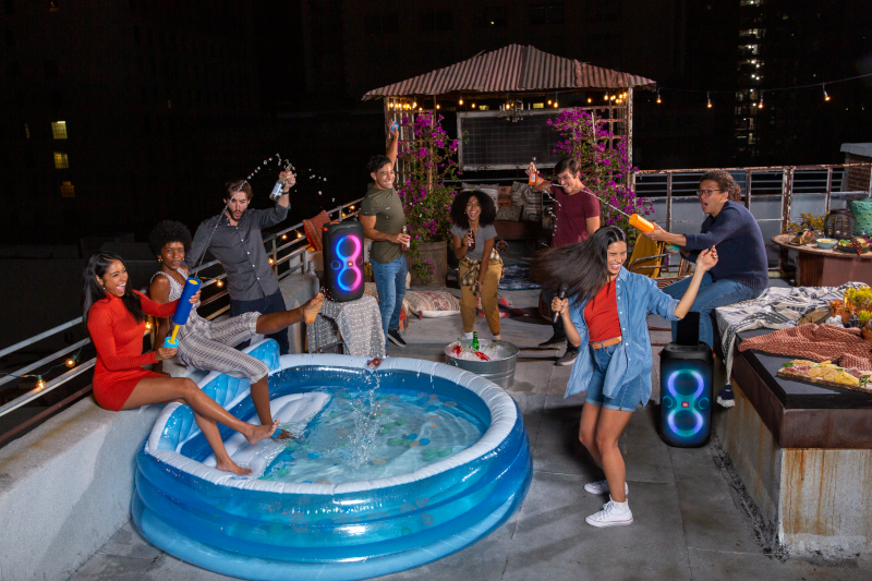 Groep mensen op een dak, sommigen in een zwembad, vieren met drankjes en muziek.