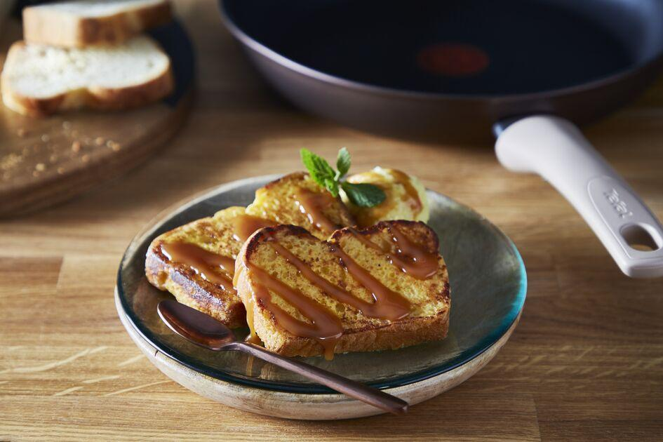 French toast with caramel sauce on a plate. A pan with a handle is in the background.