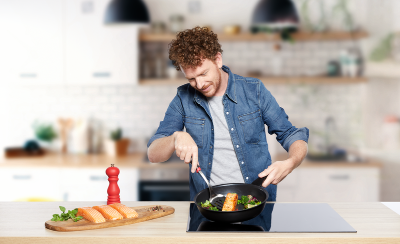 Een man die zalm met groenten bakt in een koekenpan. Keukenomgeving met ingrediënten op een plank.