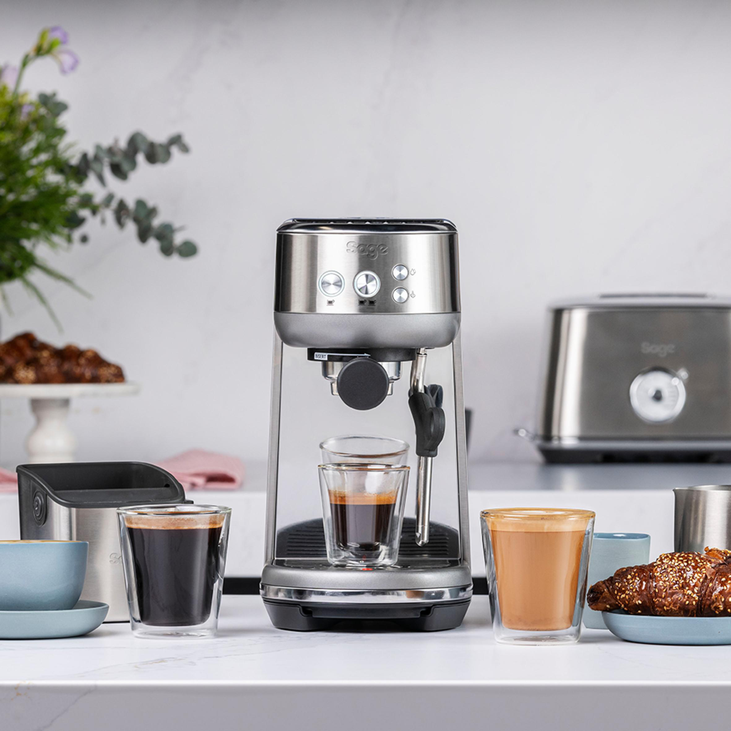 Espressomaschine mit zwei Gläsern, Kaffee und Croissant. Heller Hintergrund.