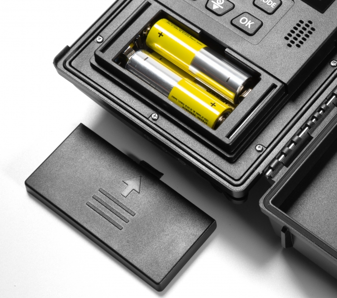 Offenes Batteriefach mit zwei gelben AA-Batterien in einem schwarzen Gerät.
