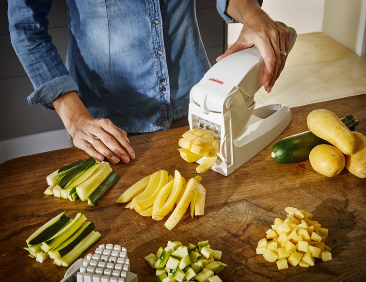 Persoon gebruikt witte groentesnijder. Courgette en aardappelen.