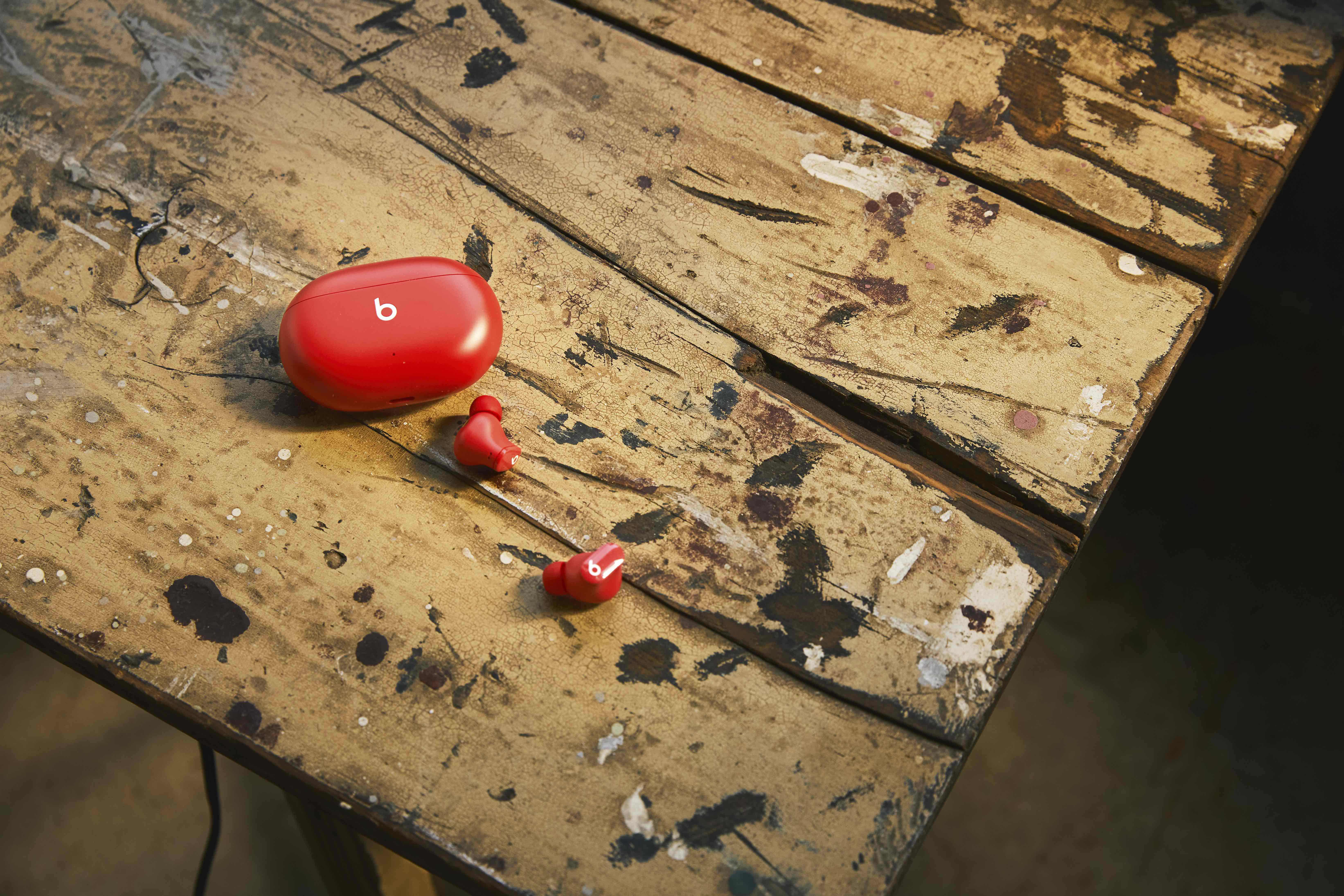 Rote Beats-Ohrhörer und Ladecase auf einem Holztisch.