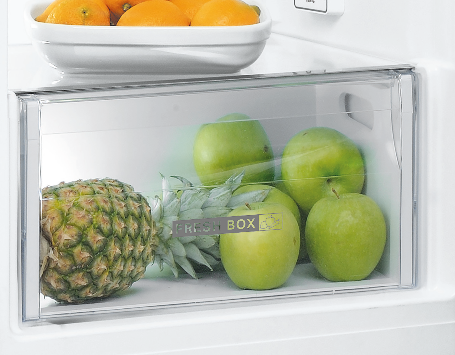 Een koelkastlade met appels en een ananas, met sinaasappels erbovenop.