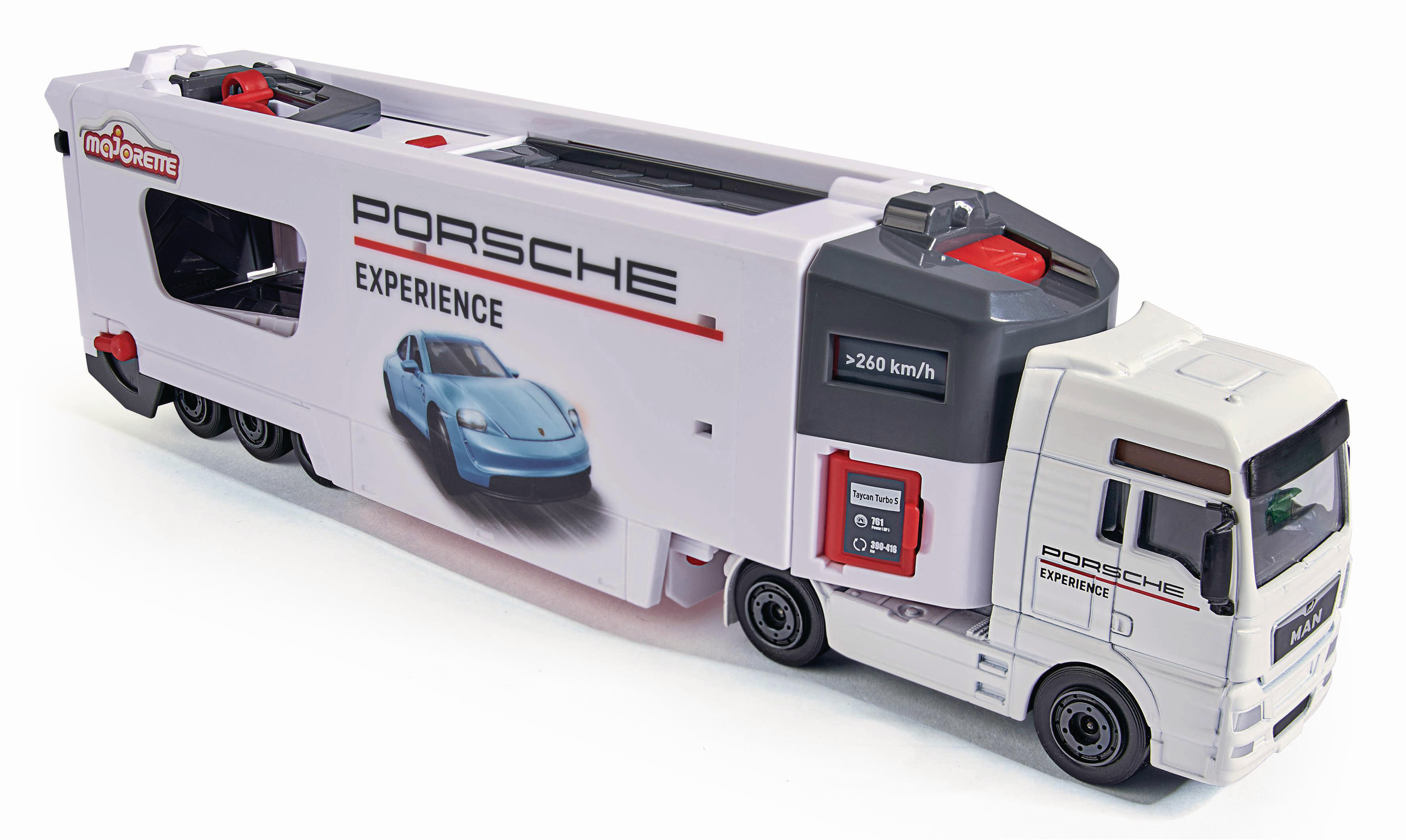 Ein weißer Porsche Experience Spielzeug-LKW mit einem blauen Auto an der Seite. Der LKW hat schwarze Räder und rote Details.