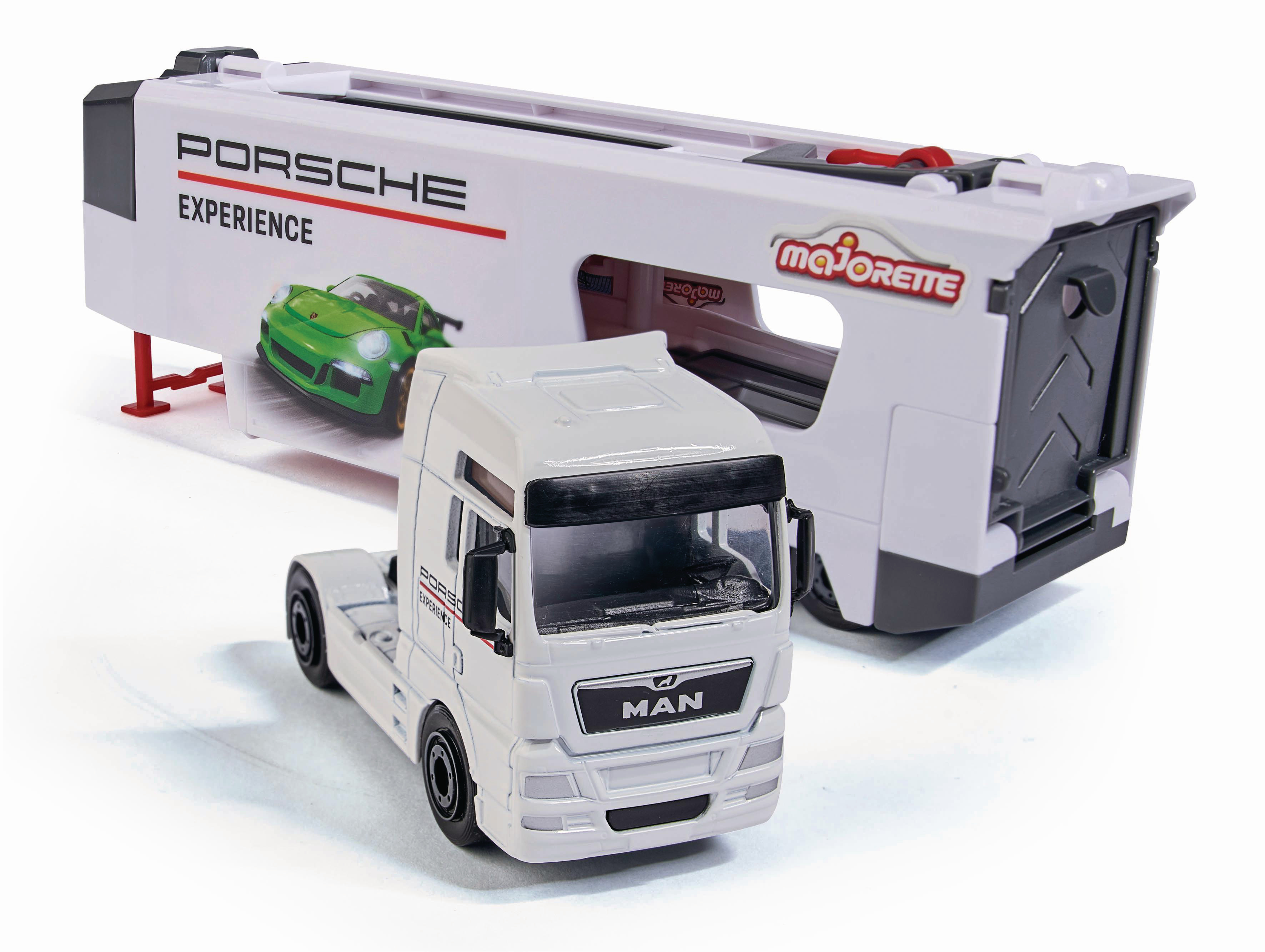 Ein weißer Spielzeug-LKW mit Anhänger mit Porsche-Branding. Ein grüner Porsche befindet sich im Anhänger. Der LKW steht auf einer weißen Oberfläche.