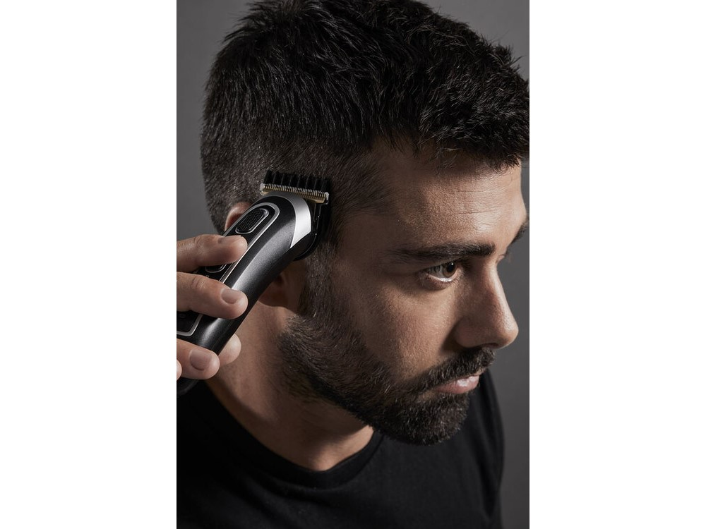 Hombre cortándose el pelo con una cortadora de pelo negra y plateada.