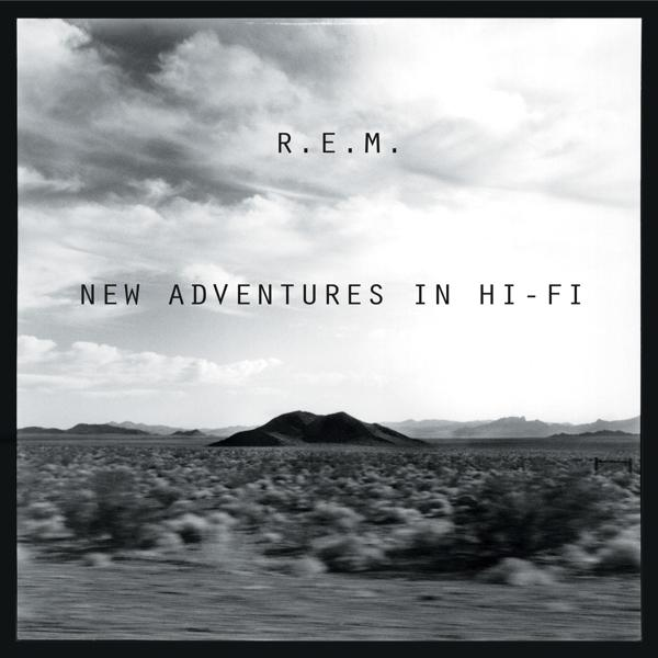 Couverture de l'album : R.E.M. sur une route. Image en noir et blanc avec un vaste paysage et un ciel nuageux.