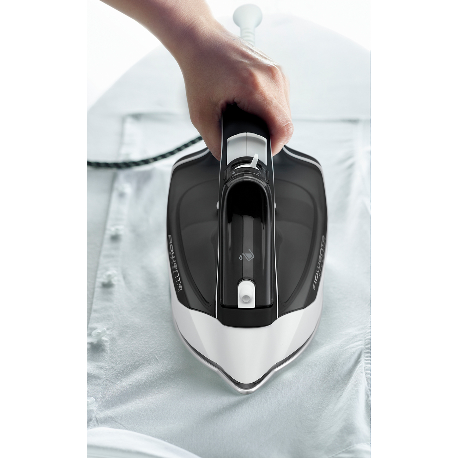 Ferro da stiro in bianco e nero che stira una camicia bianca. Mano tiene il ferro.