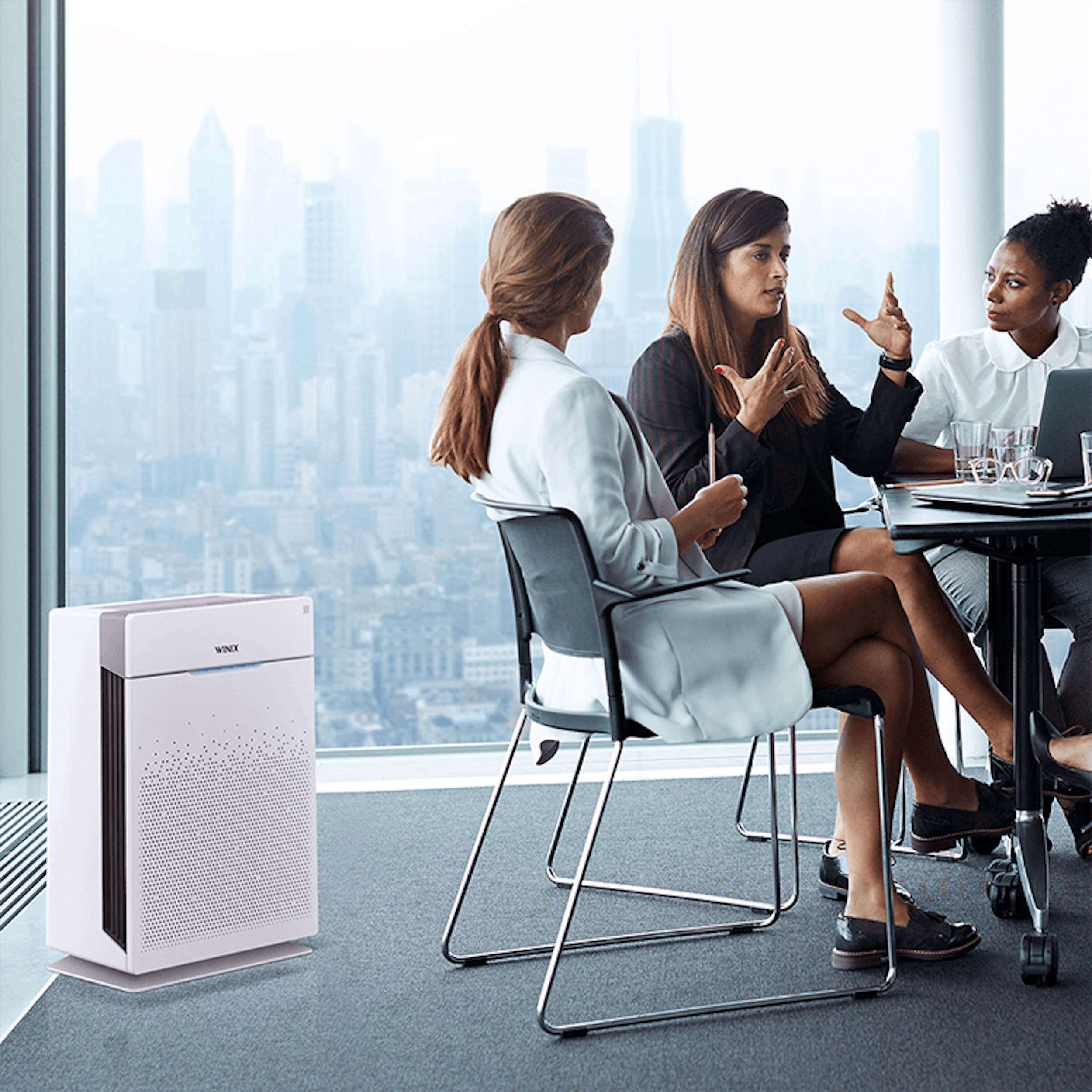 Drei Frauen sitzen an einem Tisch in einem Büro. Luftreiniger im Hintergrund.