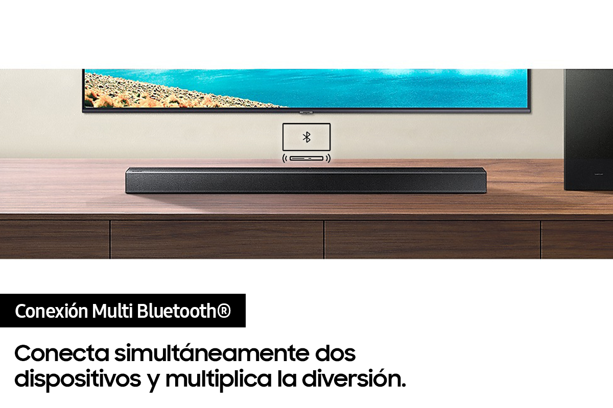 Barra de sonido negra sobre mesa de madera, bajo TV. Fondo blanco.