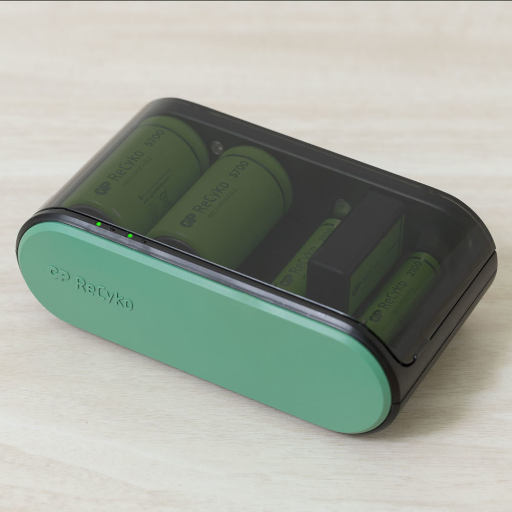 Chargeur de batterie noir et vert avec batteries à l'intérieur, sur une surface en bois.