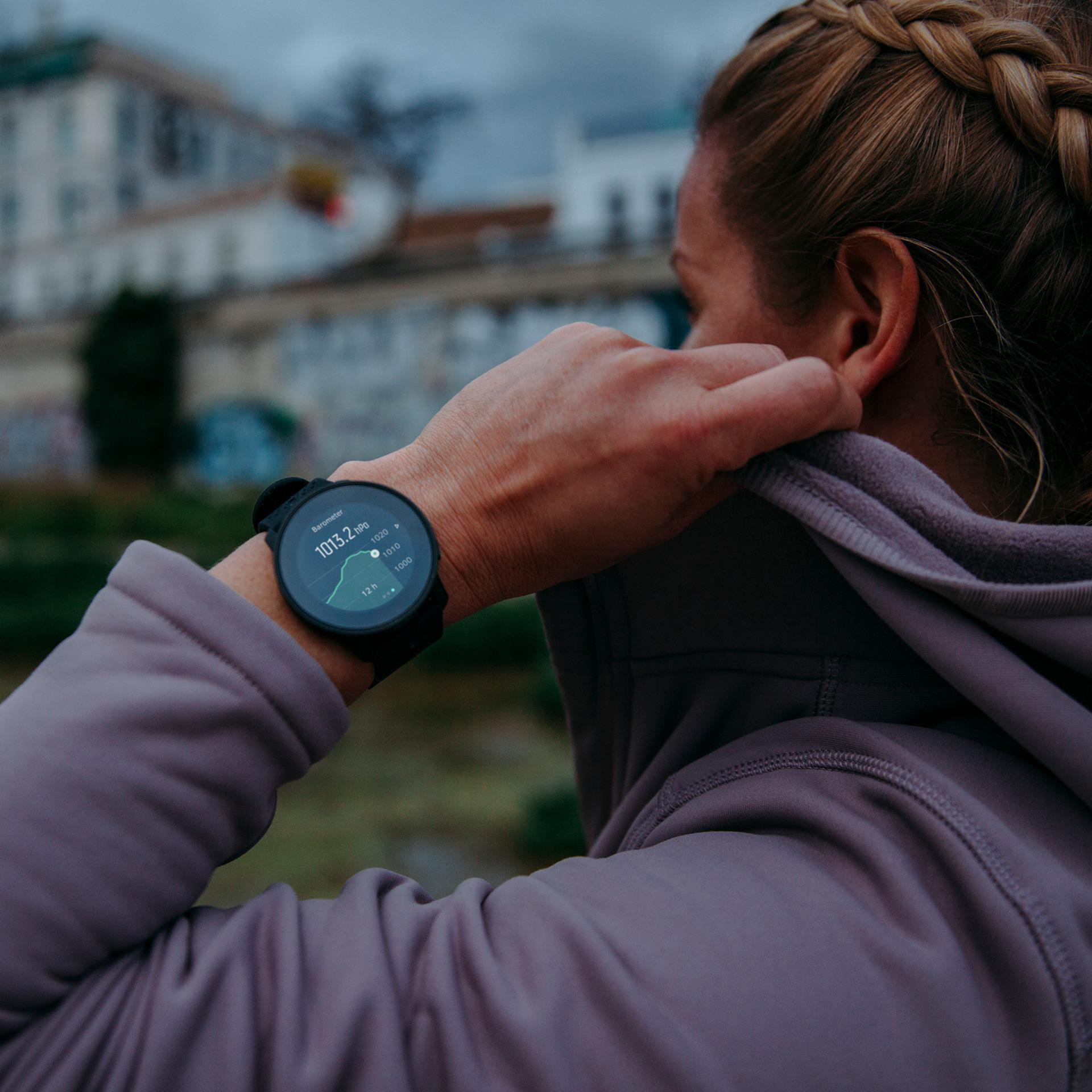 Frau mit lila Kapuzenpullover, die auf eine Uhr am Handgelenk schaut.