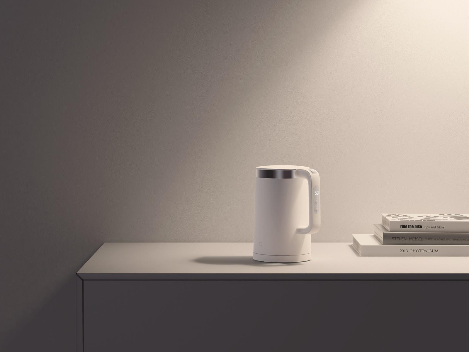 Weißer elektrischer Wasserkocher mit Digitalanzeige, auf weißer Oberfläche mit Büchern.