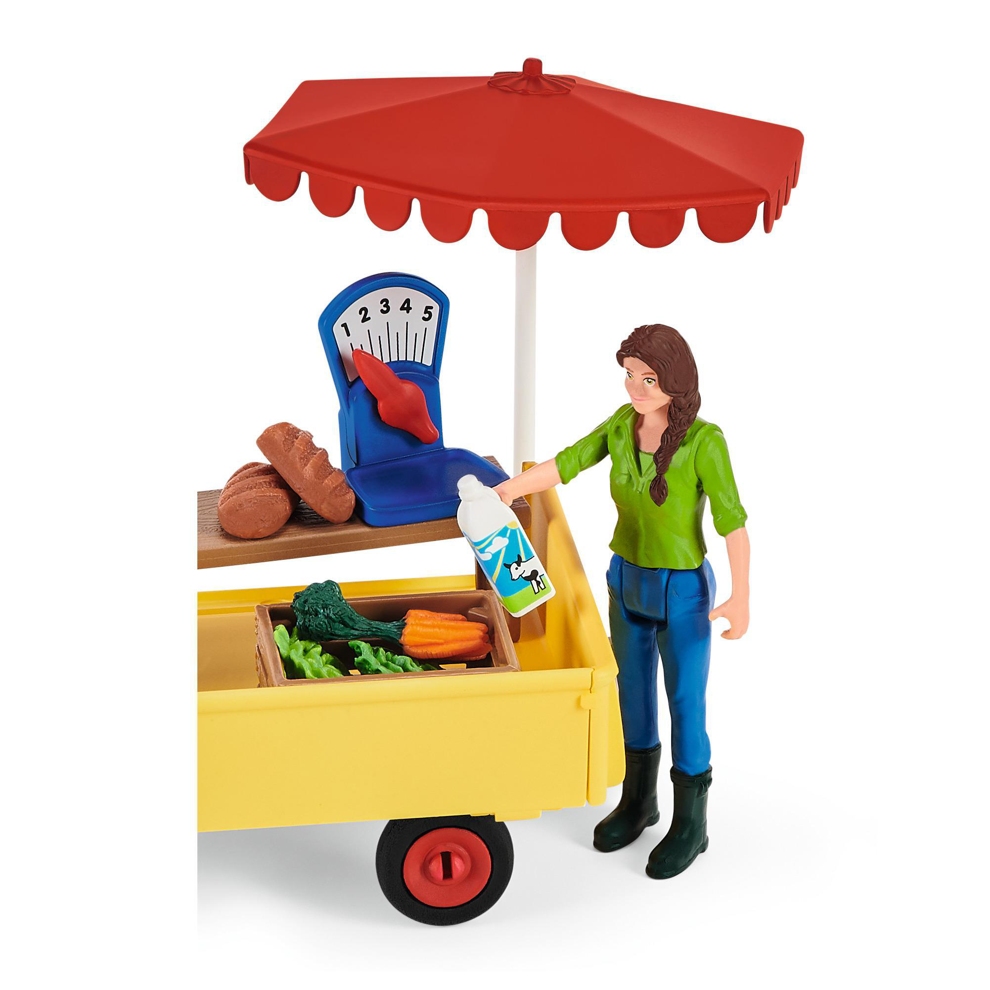Ein Spielzeugmarkt mit einer Frau, einem Wagen und Produkten. Ein roter Schirm beschattet die Szene. Karotten und Brot sind sichtbar.