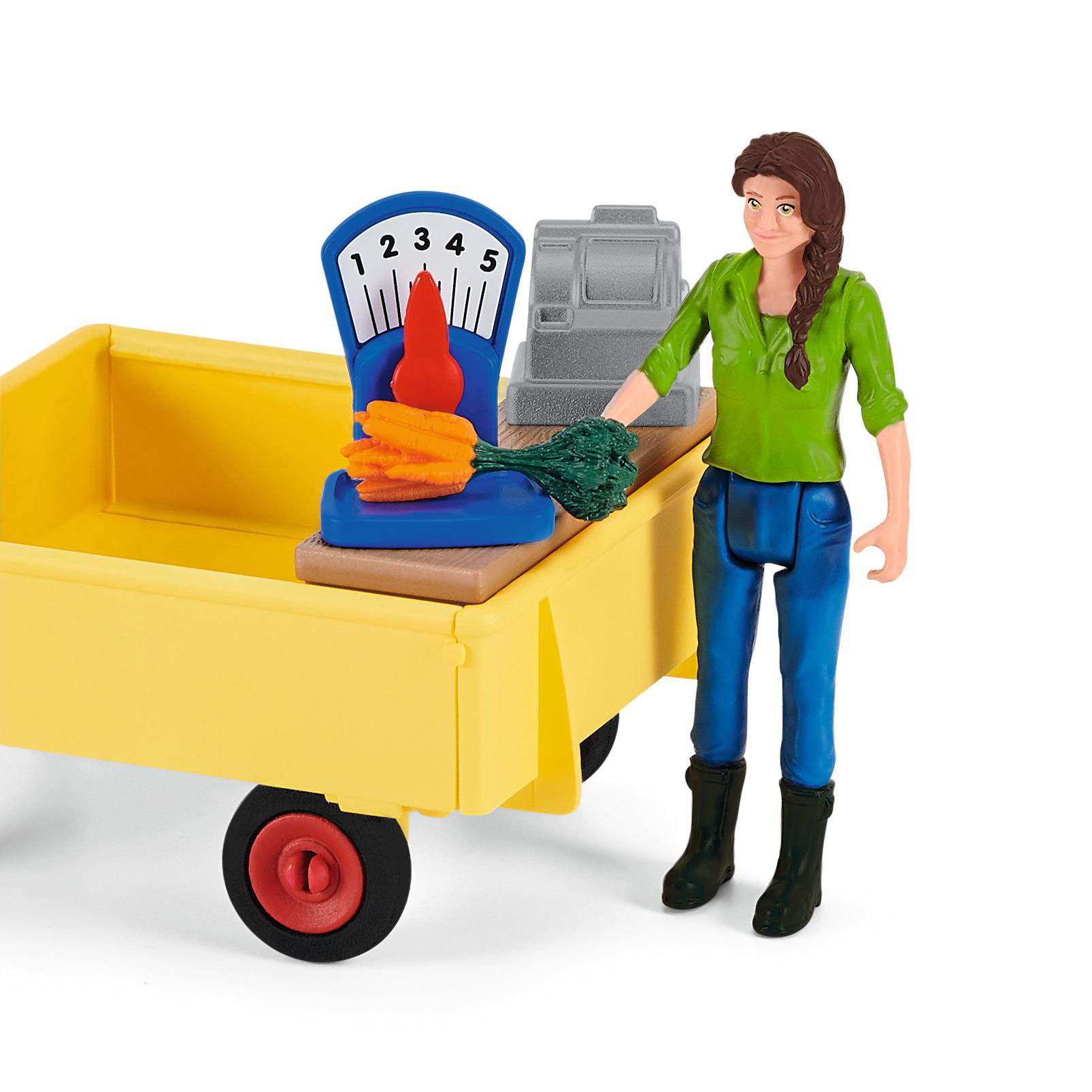 Eine Spielzeugmarktszene. Eine Frau steht an einem Wagen mit Produkten. Eine Waage und ein paar Karotten sind auf dem Wagen.