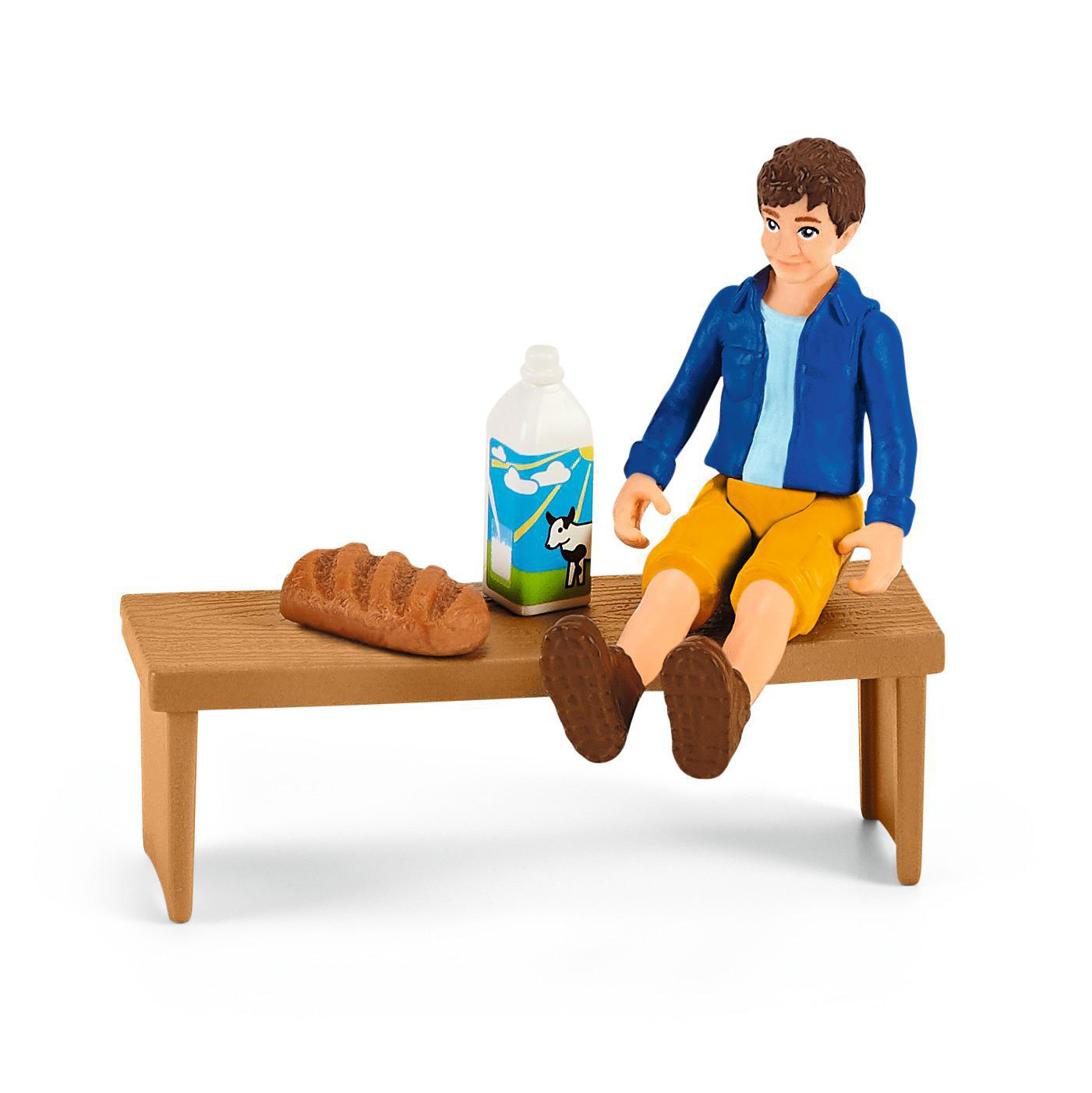 Eine Figur eines Jungen mit einer Milchflasche und Brot auf einer Holzbank.