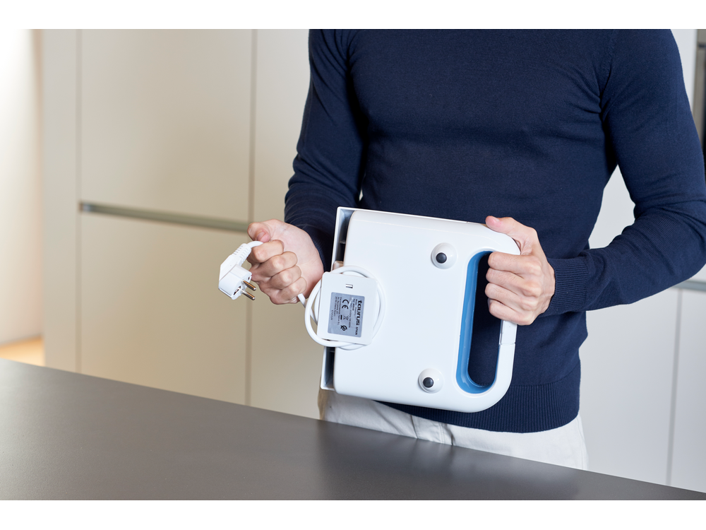 Una persona sosteniendo un electrodoméstico blanco con un asa azul, con enchufe y cable conectados.