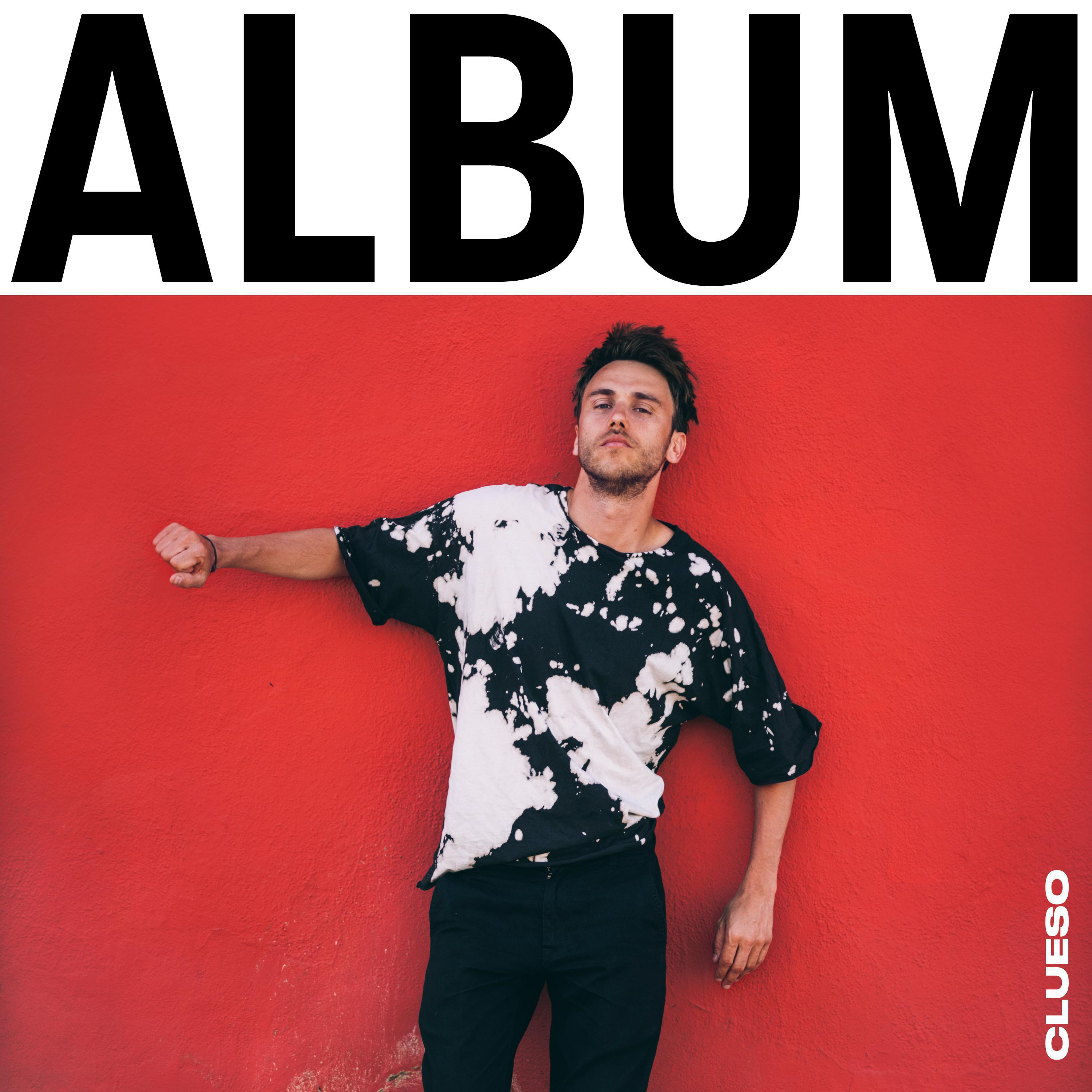 Albumcover mit einem Mann in Batik-Shirt vor roter Wand.