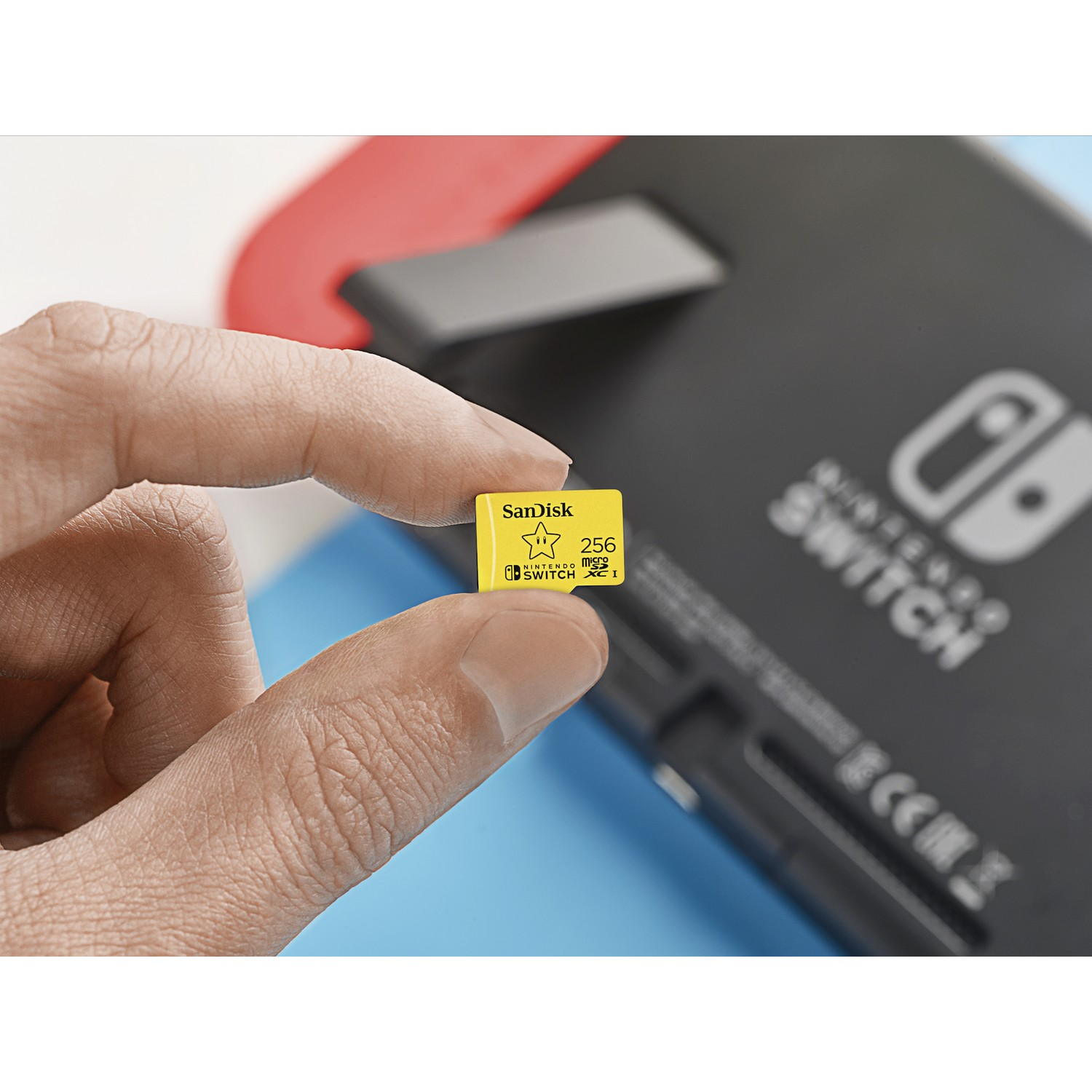 Mano sosteniendo una tarjeta microSD Sandisk de 256 GB cerca de una Nintendo Switch negra.
