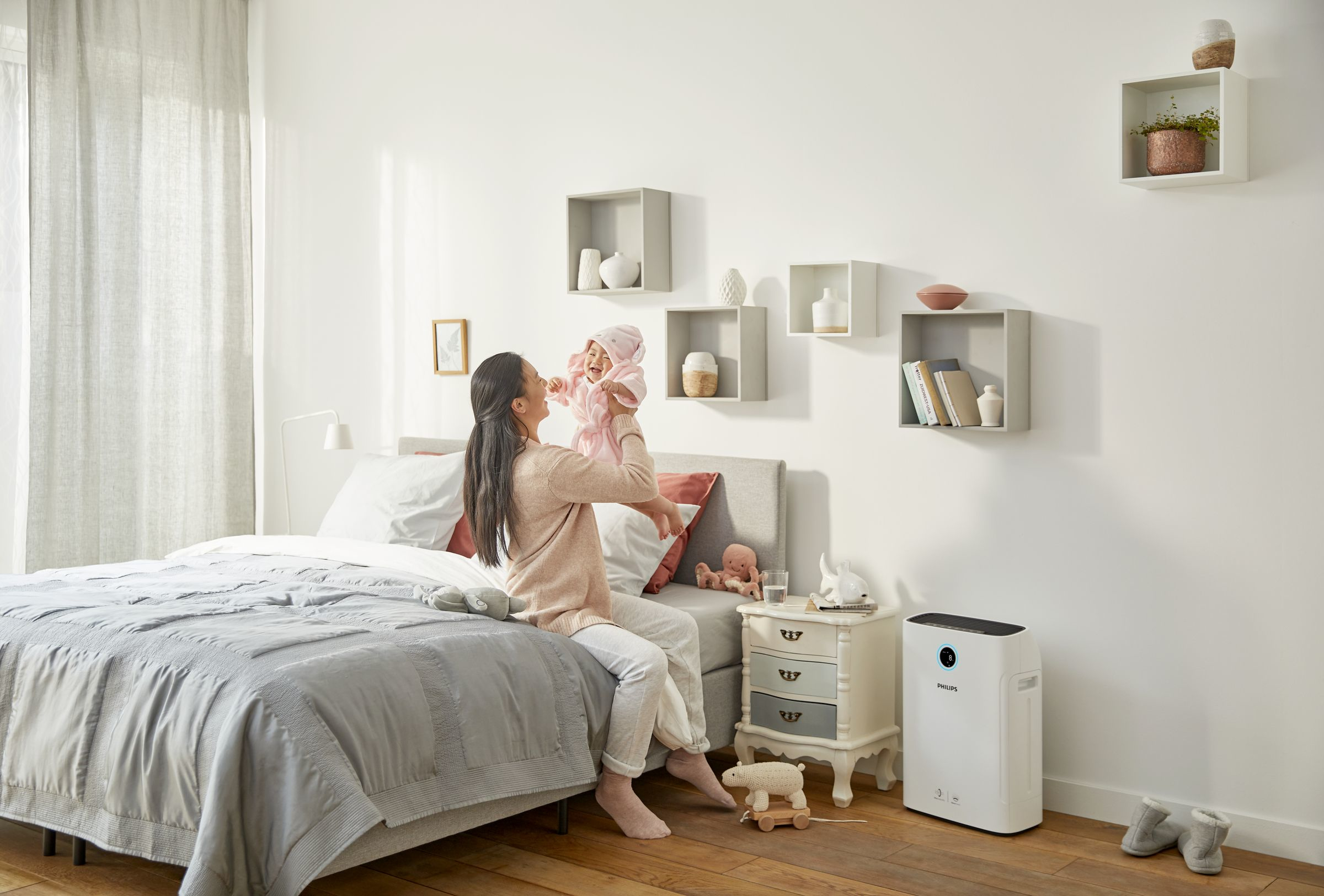 Una madre che gioca con il suo bambino in una camera da letto luminosa. Purificatore d'aria a terra.
