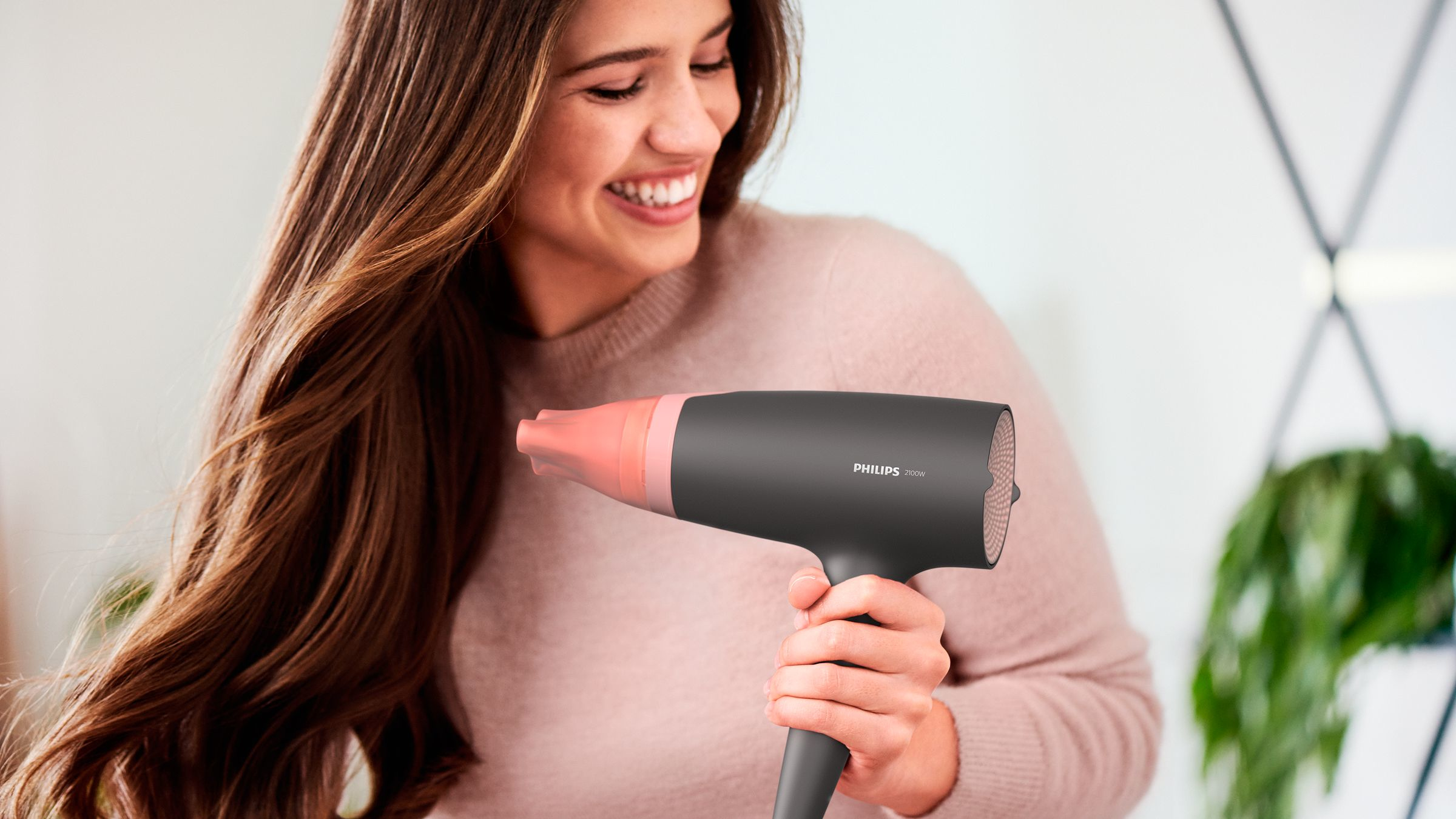 Une femme souriante, tenant un sèche-cheveux Philips, avec de longs cheveux bruns au vent.