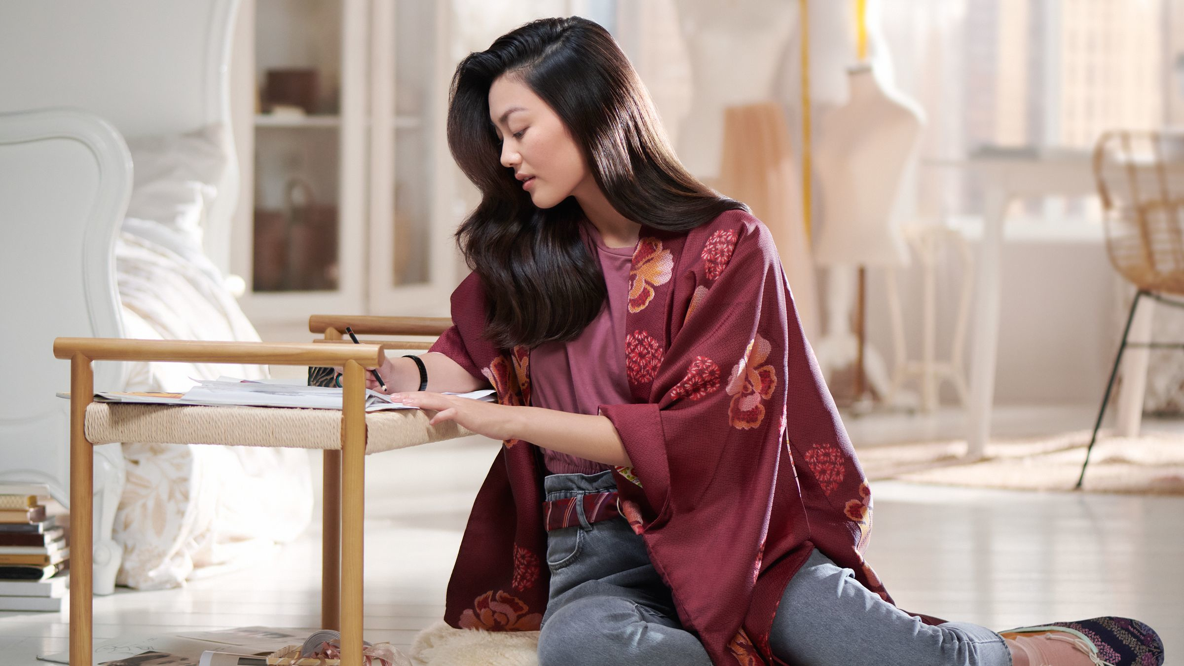 Femme en kimono bordeaux assise, écrit sur papier. Un banc et une chambre en arrière-plan.