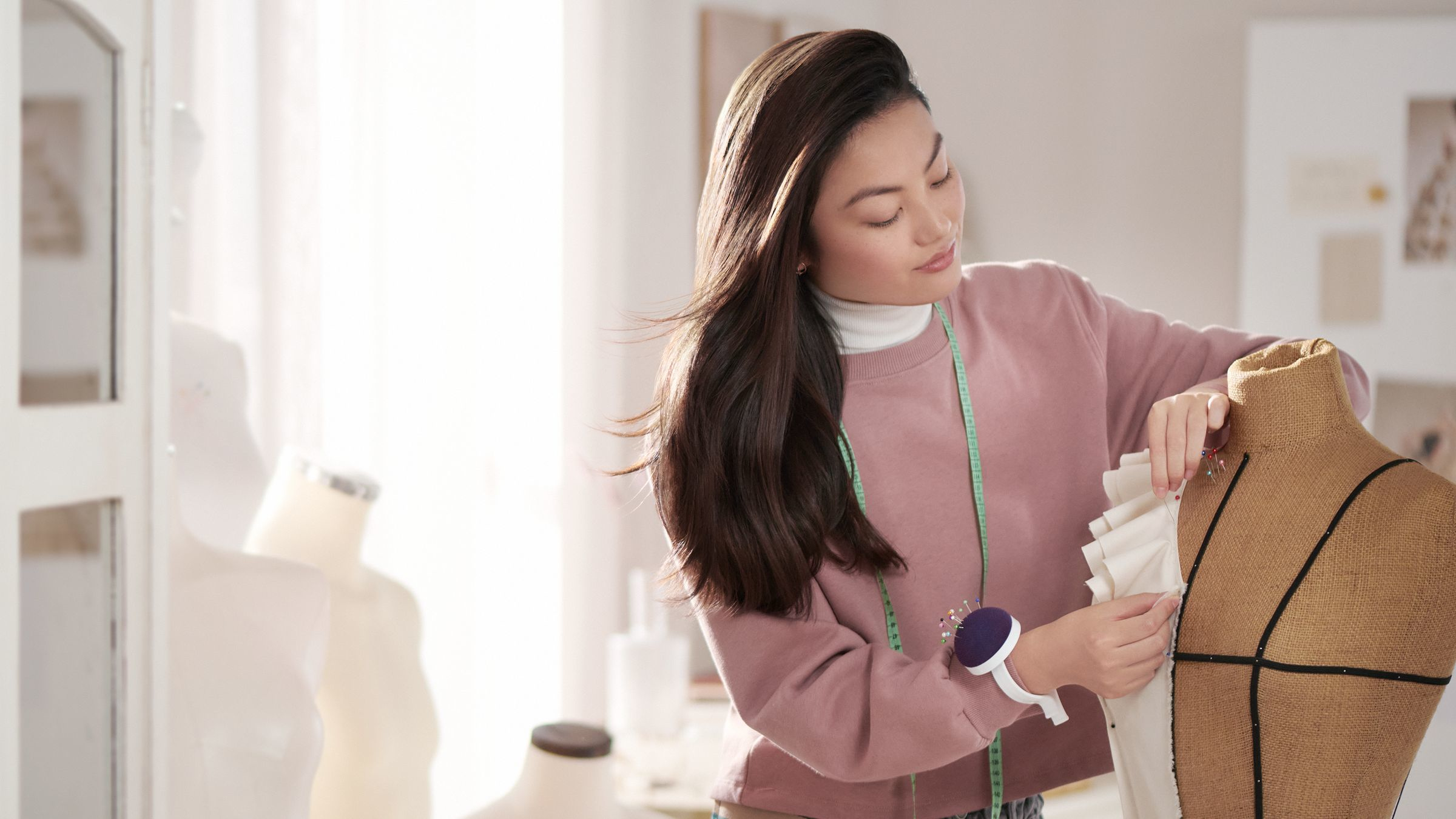 Une femme en pull rose épingle du tissu sur un mannequin.