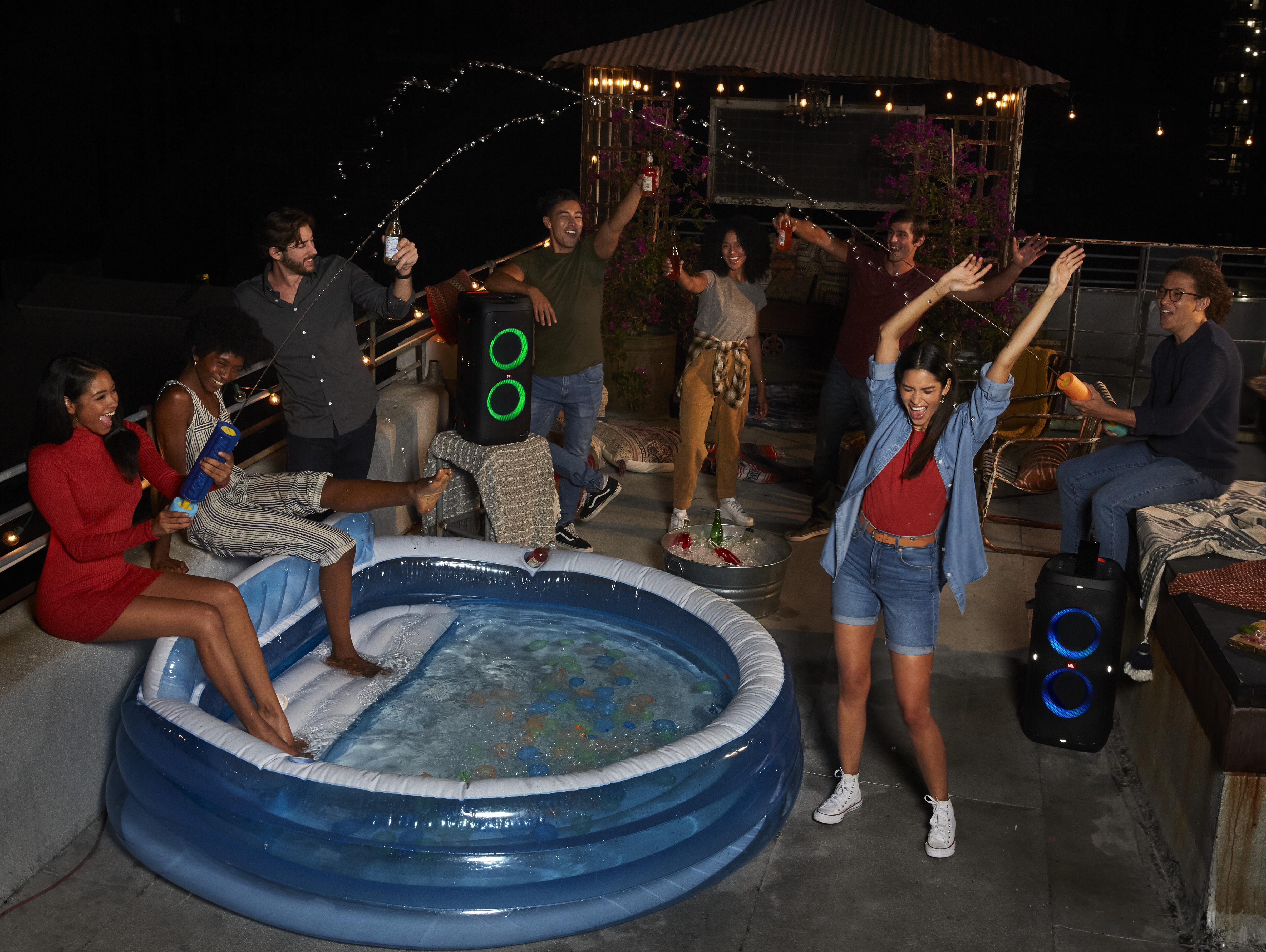Leute auf einem Dach bei Nacht, feiern um einen kleinen Pool. Lautsprecher sind sichtbar. Einige planschen.