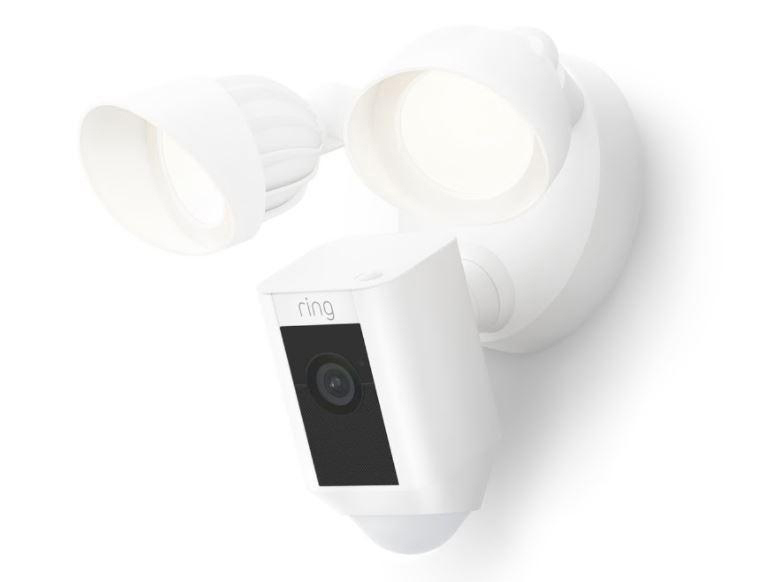 Weiße Ring-Überwachungskamera und Flutlichter. Es ist an einer Wand montiert, mit schwarzem Kameraobjektiv.