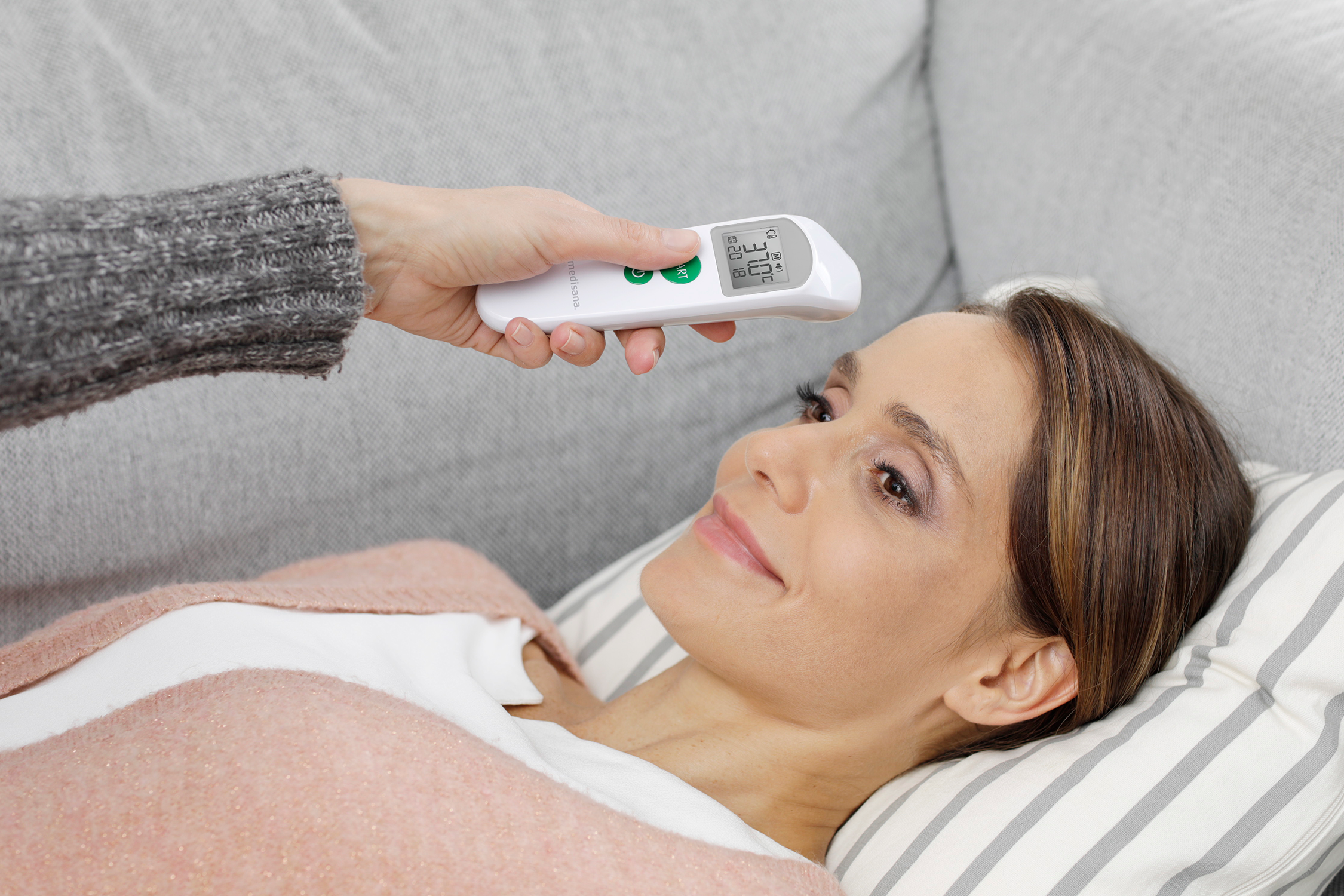 De temperatuur van een vrouw wordt gemeten met een digitale thermometer. Ze ligt op een bank.