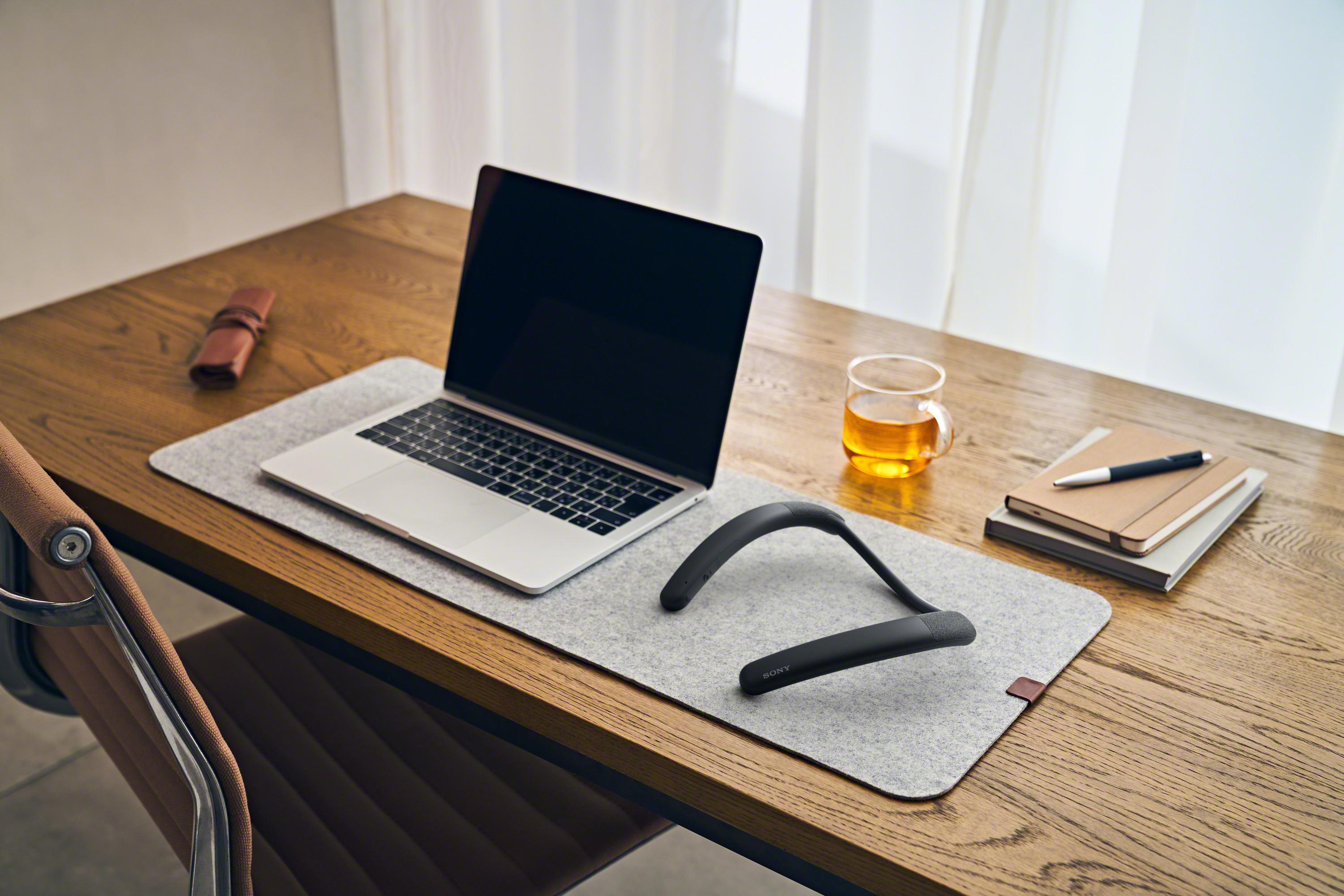 Laptop, Nackenband, Glas Tee, Notizblock, Stift auf einem Holzschreibtisch.