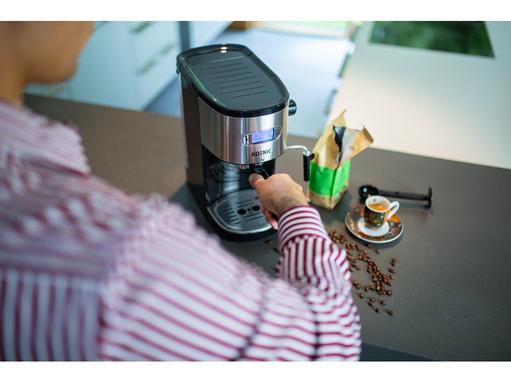 Una persona preparando café. Cafetera, granos de café y taza de espresso en la encimera.