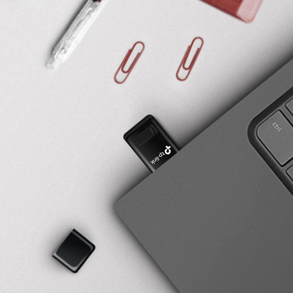 Laptop mit eingestecktem USB-Laufwerk. Büroklammern und ein kleiner schwarzer Koffer sind in der Nähe.