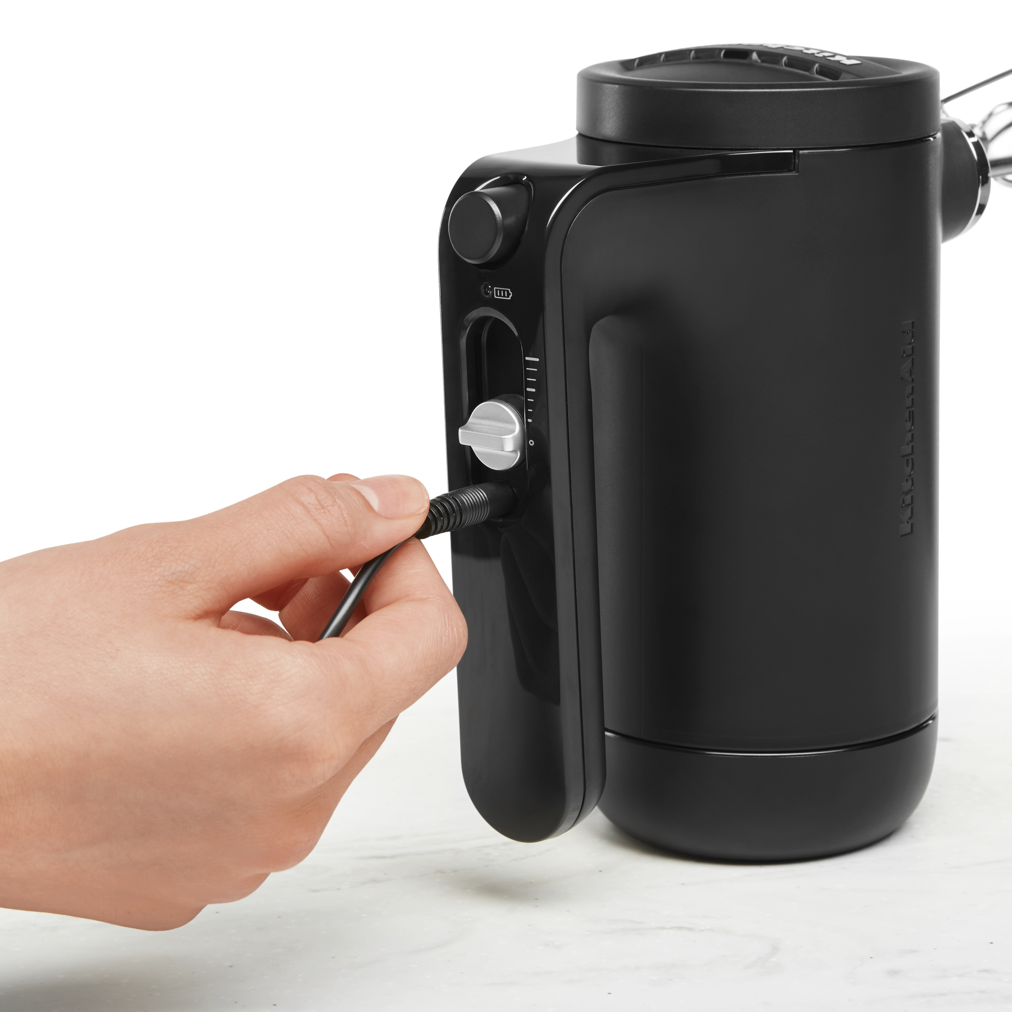 Eine Hand steckt ein Ladekabel in einen schwarzen KitchenAid Handmixer.