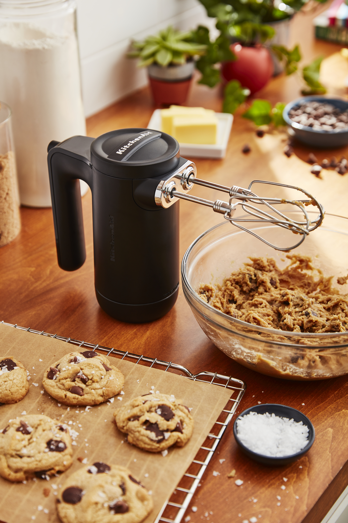Ein schwarzer KitchenAid Handmixer mit Keksen und Keksteig auf einer Holzoberfläche.