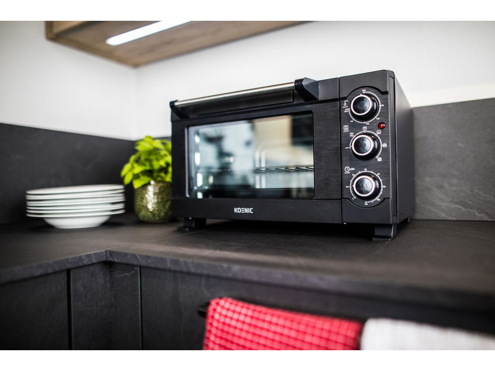 Un horno negro en una encimera con una planta y platos al lado, ambiente de cocina.